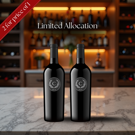 Two black wine bottles with a logo on a marble surface, with a blurred bar background.