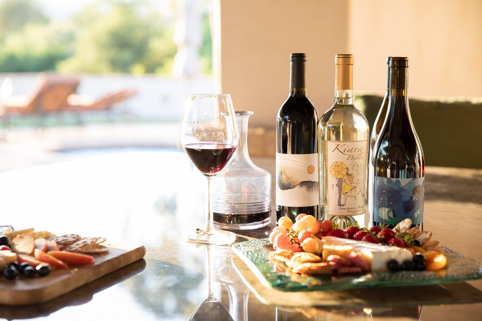 Three bottles of wine next to a glass and cheese board