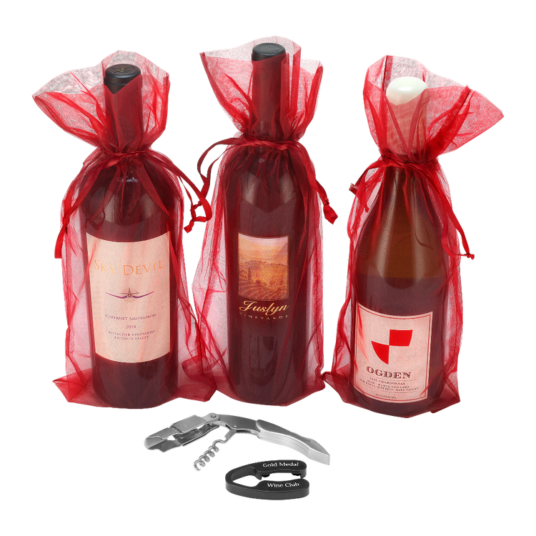 Three bottles of wine in red sheer gift bags next to wine tools