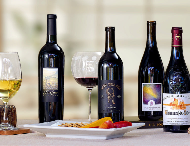 Row of wine bottles on a table with glasses and food in a home setting